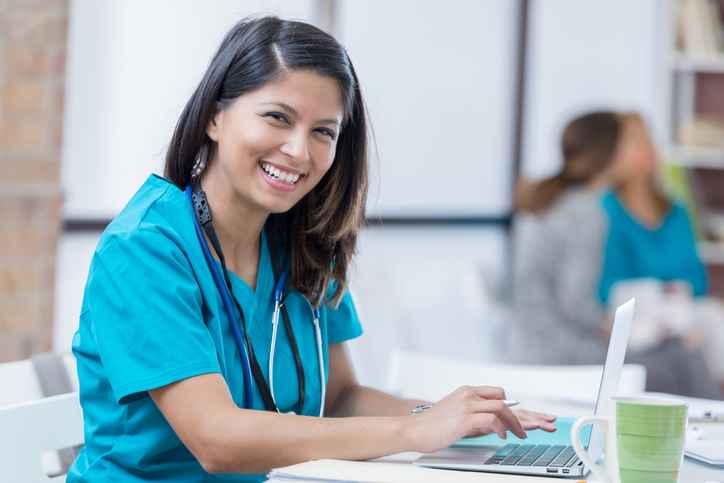 A smiling nurse in Shreveport, LA, is working on her laptop to log in to the employee portal.