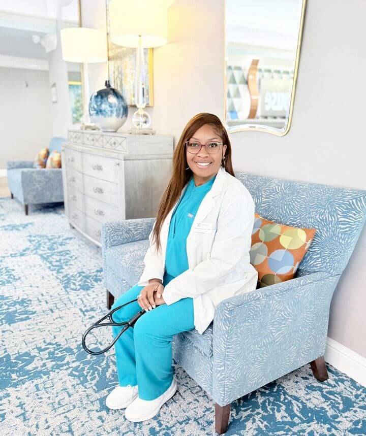 A woman in scrubs sits on a blue couch at The Guest House Skilled Nursing and Rehabilitation