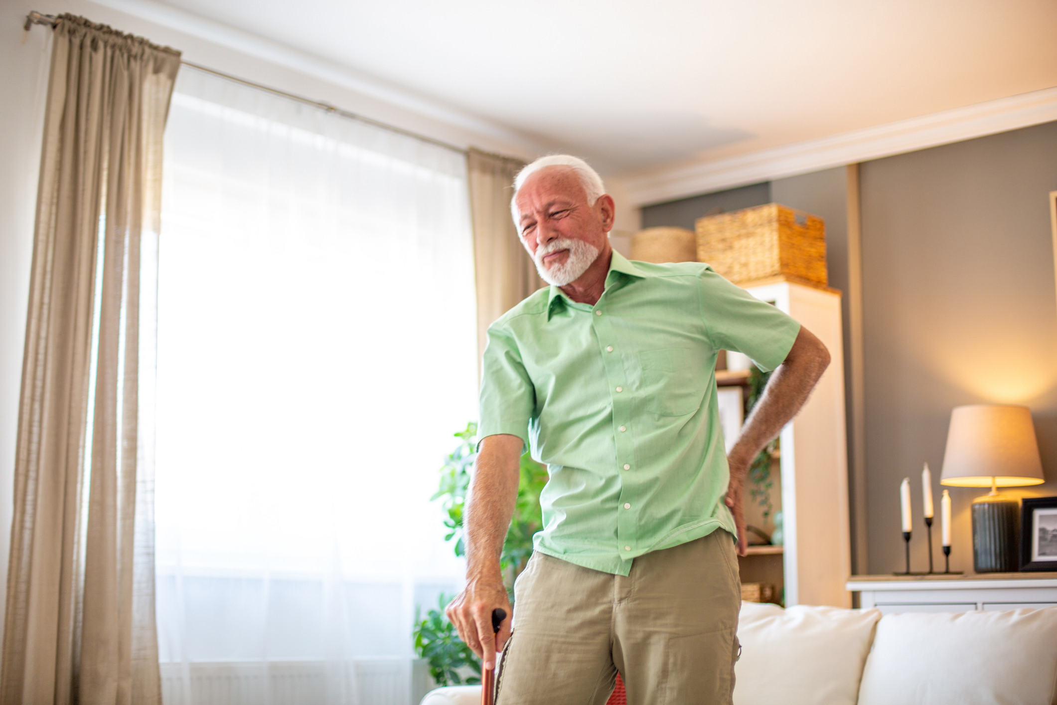 Senior man holding walking cane and experiencing back pain at home